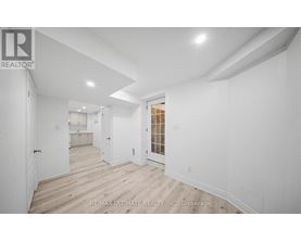 A white room with wood flooring and a doorway leading to another room.