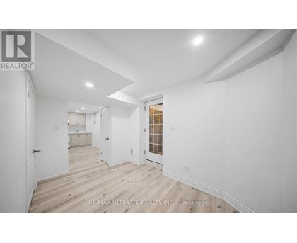 A white room with wood flooring and a doorway leading to another room.