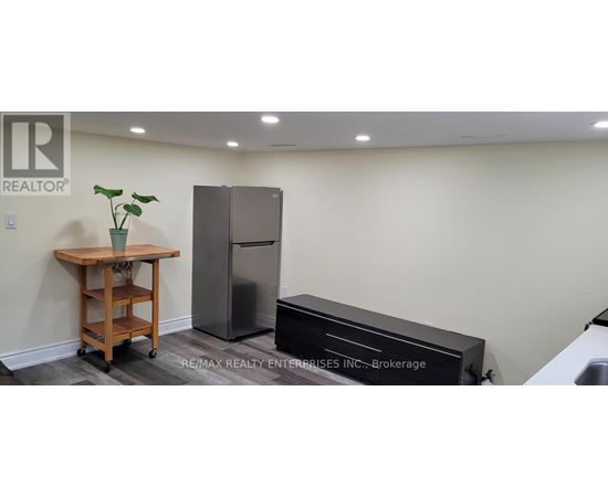 A kitchen area with a refrigerator, a wooden cart with a plant on it, and a black countertop.