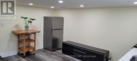 A kitchen area with a refrigerator, a wooden cart with a plant on it, and a black countertop.