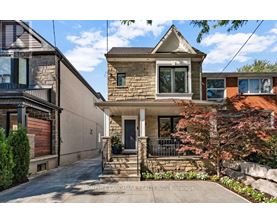 A house with a stone facade and a front porch is surrounded by a well-kept garden.