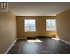A spacious room with two windows and wooden flooring.
