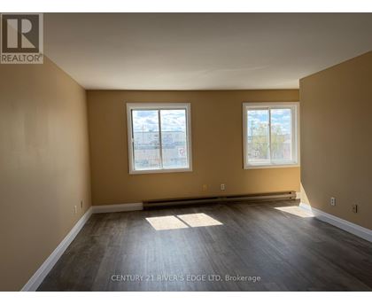 A spacious room with two windows and wooden flooring.