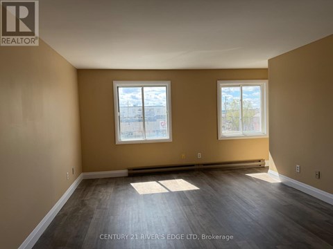 A spacious room with two windows and wooden flooring.