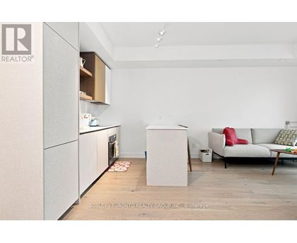 A kitchen with a refrigerator, oven, and a couch in the living room.