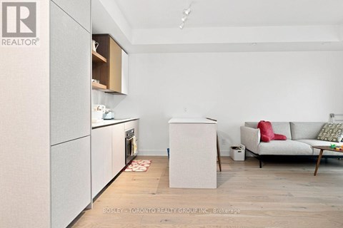 A kitchen with a refrigerator, oven, and a couch in the living room.