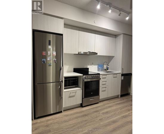 A modern kitchen with a stainless steel refrigerator and wooden flooring.