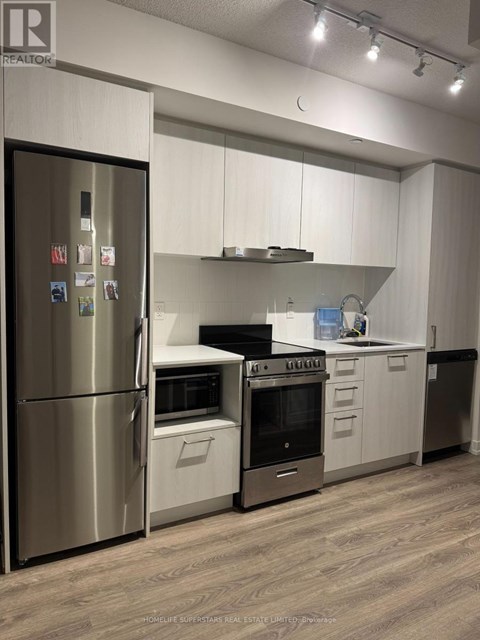 A modern kitchen with a stainless steel refrigerator and wooden flooring.