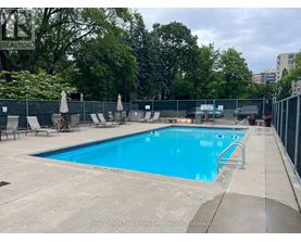 A large outdoor swimming pool surrounded by a fence and lounge chairs.
