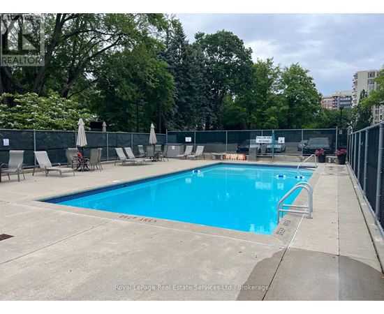 A large outdoor swimming pool surrounded by a fence and lounge chairs.