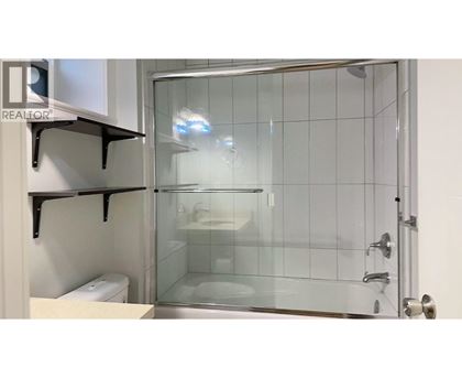 A glass shower stall with a glass door and a white toilet in the corner.