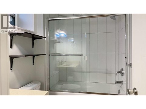 A glass shower stall with a glass door and a white toilet in the corner.