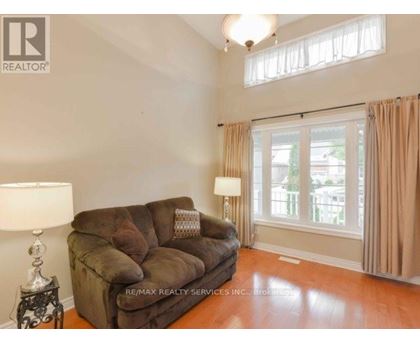 A brown couch sits in a living room with a lamp and a window.