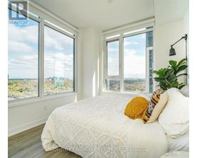 A bedroom with a large bed and a view of the city through the windows.
