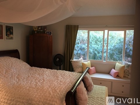 A bedroom with a bed, a window seat, and a wooden cabinet.