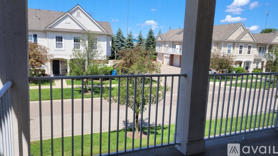 A view from a balcony overlooking a grassy area and a row of houses.