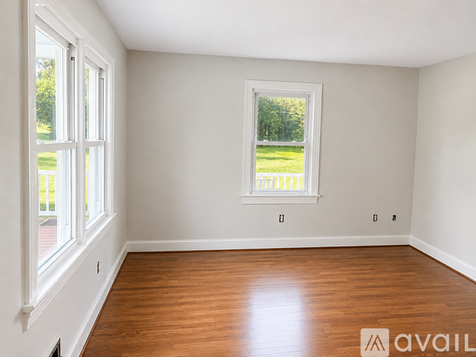 A room with a large window and wooden floors is available for rent.