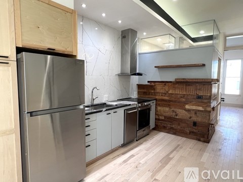 A modern kitchen with a stainless steel refrigerator and wooden flooring.