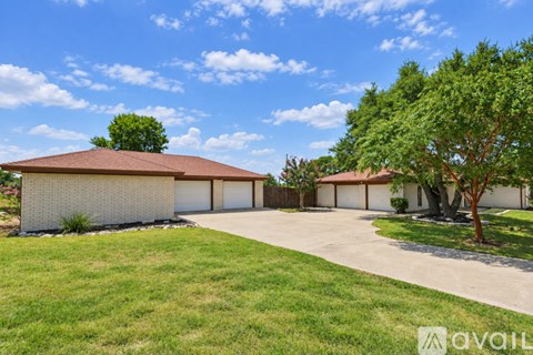 A house with a brown roof and white walls is surrounded by trees and grass.