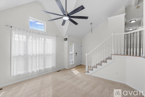 A spacious room with a fan and a staircase.