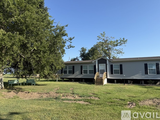 A mobile home sits in a grassy field with trees in the background.