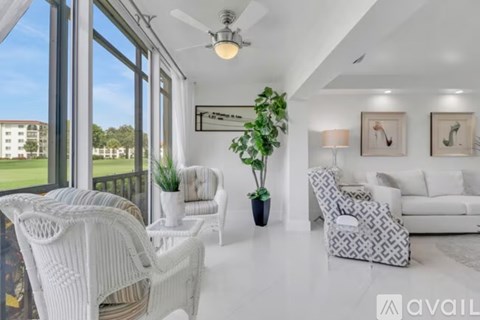 A living room with white furniture and a large window overlooking a green lawn.