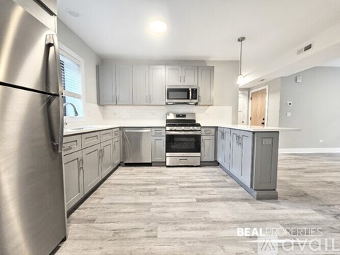 A kitchen with a refrigerator on the left and a stove top oven in the middle.
