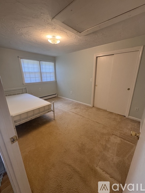 A bedroom with a bed, carpet, and a window.