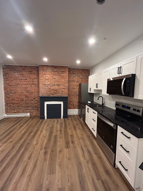 A kitchen with a brick wall and wooden floors.