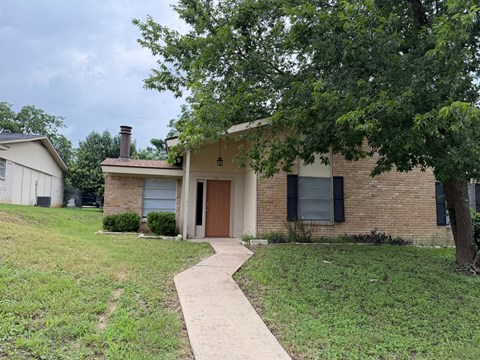 A house with a brown door and black shutters is surrounded by green grass and trees.