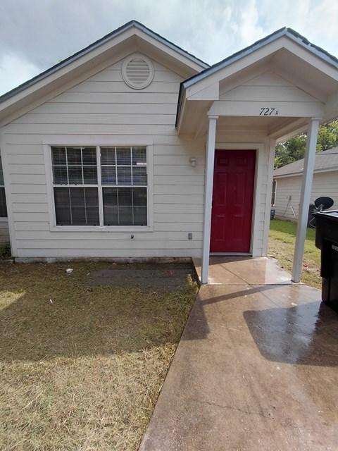 A small white house with a red door and a mailbox on the right.