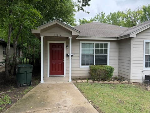 A small house with a red door and a window is in front of a green trash can.