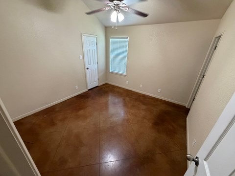 A room with brown flooring and a ceiling fan.