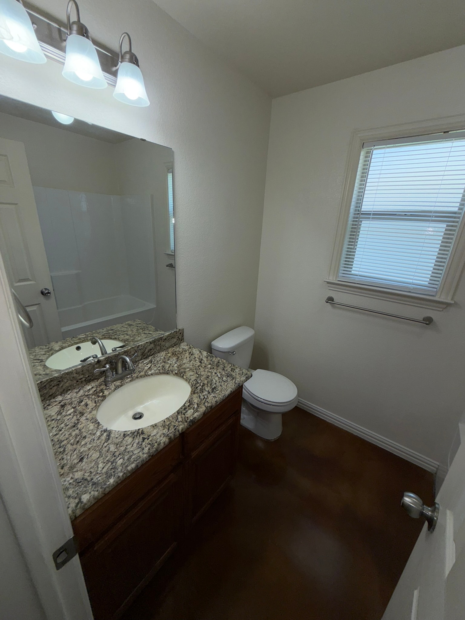 A bathroom with a toilet, sink, mirror, and a window with blinds.