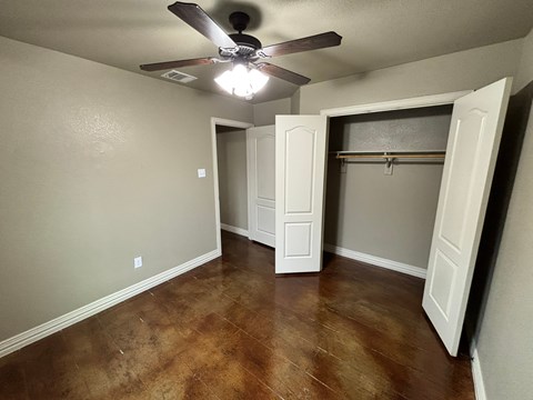 A room with a ceiling fan and brown flooring.