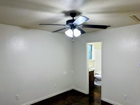A room with a ceiling fan and a doorway leading to a bathroom.