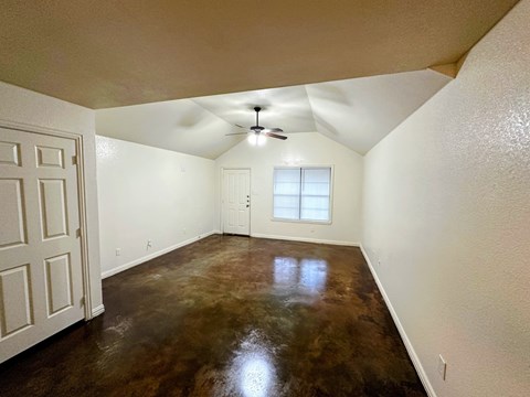 A room with a brown floor and a ceiling fan.