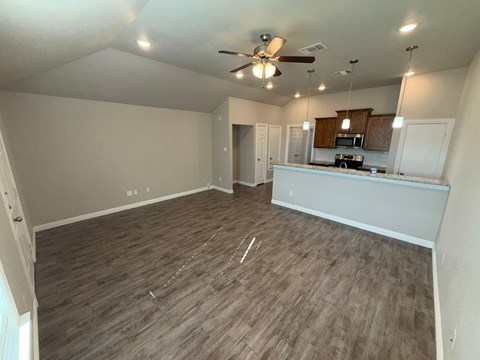 A room with a ceiling fan and a kitchenette in the background.
