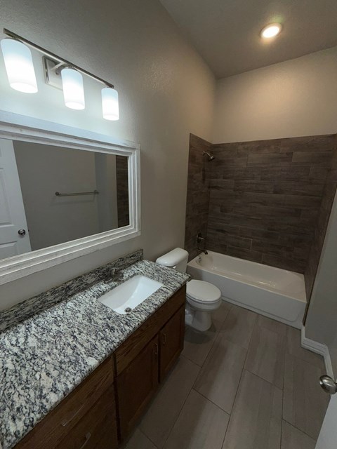 A bathroom with a granite counter top and a white toilet.