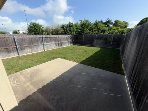 A backyard with a concrete patio and a wooden fence.