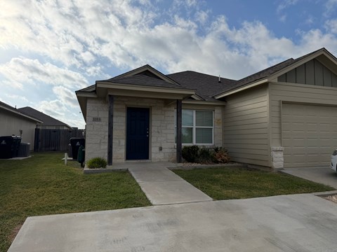 A house with a black door and a small window is in front of a fence.