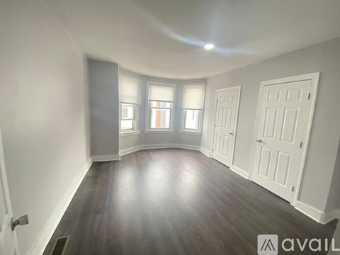 A room with wooden floors and white walls, featuring a window with a view of a building outside.