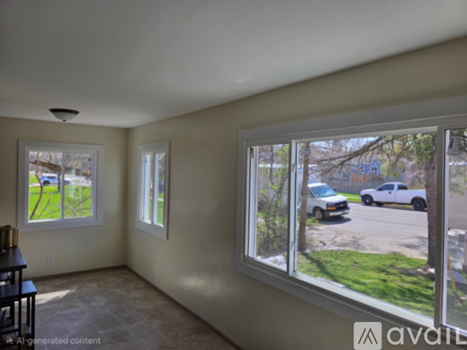 A room with a view of a street with cars and trees.