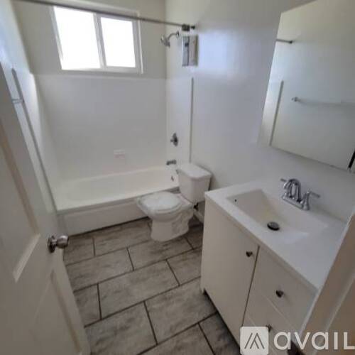 A white toilet is in a bathroom with tile flooring and a white sink.
