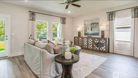 A living room with a white couch, a round table with a plant on it, and a ceiling fan.