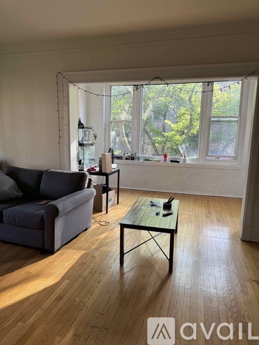 A living room with a grey couch, a glass table, and a window with a view of trees.