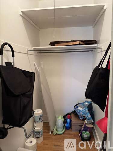 A small closet with a black bag hanging on the door and a black bag on the floor.
