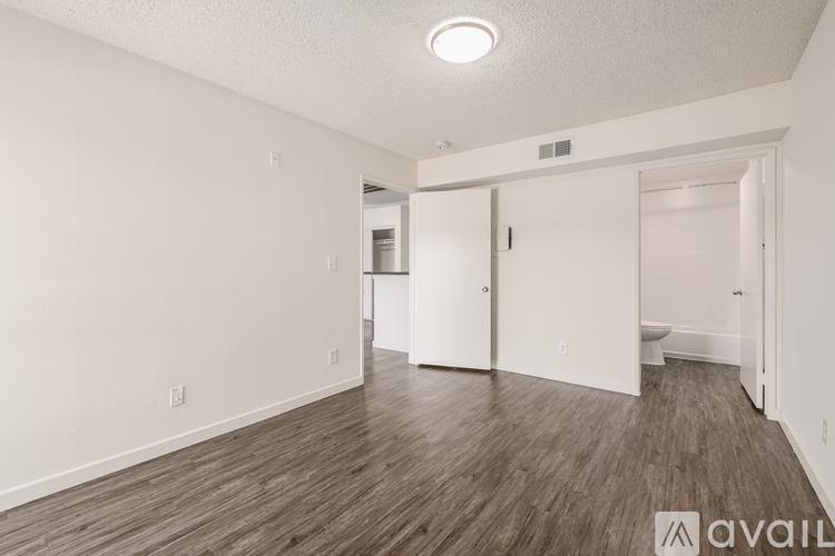 A room with wooden flooring and white walls, with a door on the right and a mirror on the left.