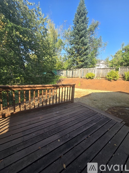 A wooden deck overlooks a backyard with a fence and trees.