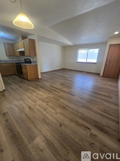A spacious room with wooden flooring and a kitchen area with cabinets and a stove.